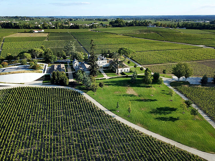 An aerial drone view of Château Cheval Blanc's castle and modern white winery surrounded by vineyards in Saint-Émilion