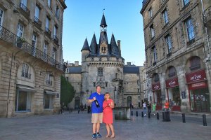 Tim holds a Bordeaux magnum and Jennifer holds a giant antique key as they pose in front of Bordeaux's Porte Cailhau
