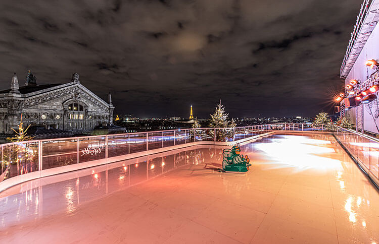 The rooftop rink at Galeries Lafayette with a view of the Eiffel Tower at nighttime in Paris