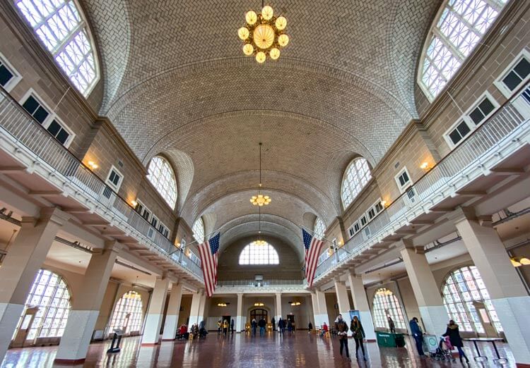 The Ellis Island Registry Room with vaulted ceiling, chandeliers and American flags hanging