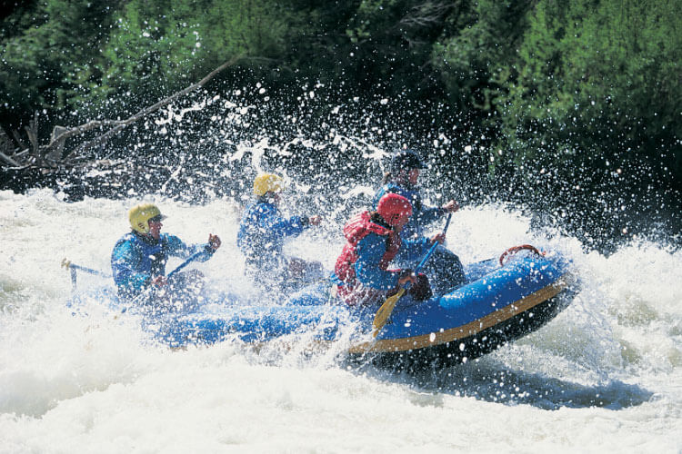 A group of white water rafters paddle through spray on a rapid