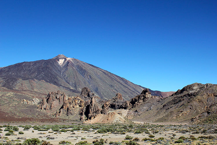 A view of Mount Teide with its snowy cone and the Roques de García rock formations standing in front as seen from a distance