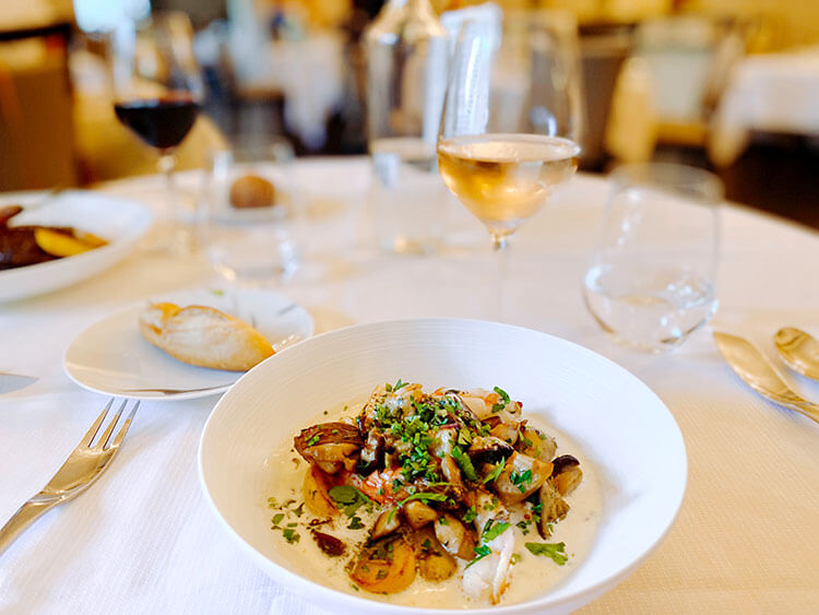 A table with a bowl and glass of rosé wine, and in the bowl is cassolette with cepes and langoustines