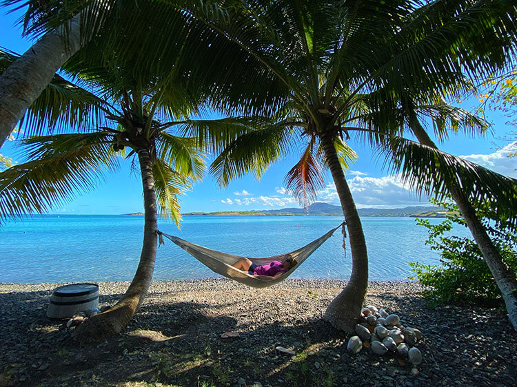 Jennifer relaxes in a hammock strung between two palm trees with the blue sea behind her on Ilet Oscar in Martinique 