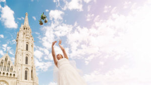 A bride throughs her bouquet high in the air with a European church in the background