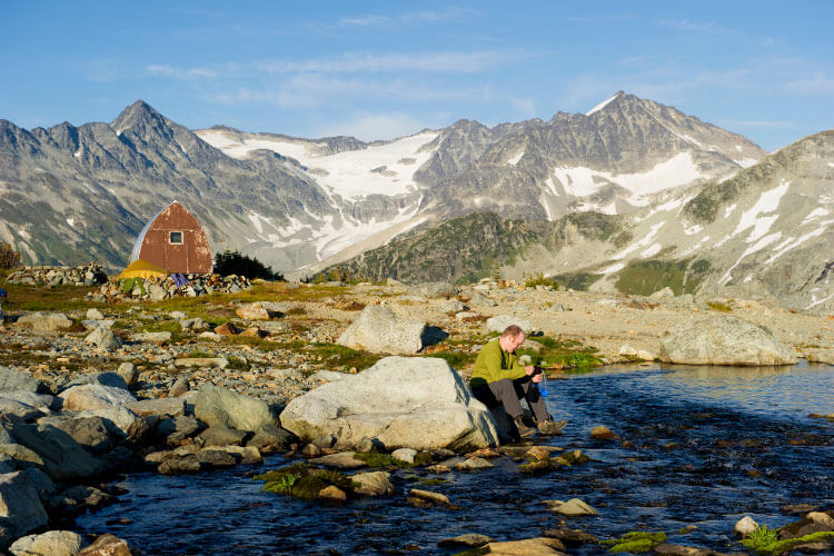 A hiker uses a travel water filter in a mountain lake