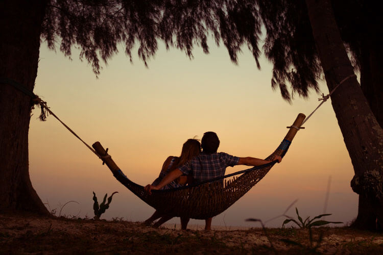 A couple watches sunset from a hammock together