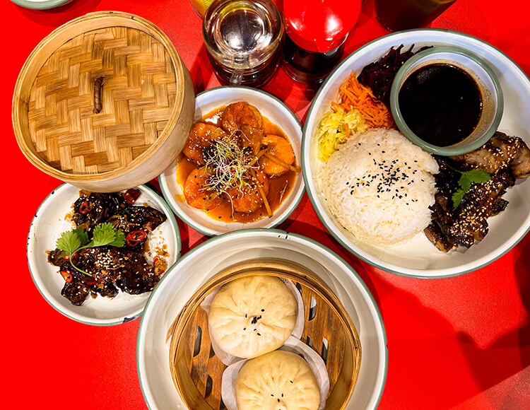 A selection of dishes at NaiNai including bao buns served in a steamer basket, fried eggplant and pork with rice