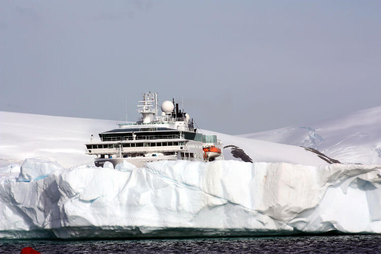 An expedition ship cruises behind an iceberg in Antarctica