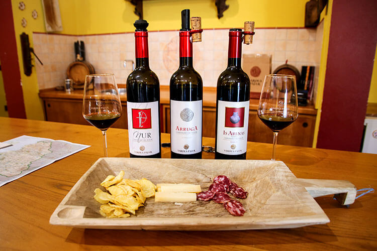 Three bottles of wine with local cheese and salumi at Cantina Sardus Pater in Sant'Antioco, Sardinia