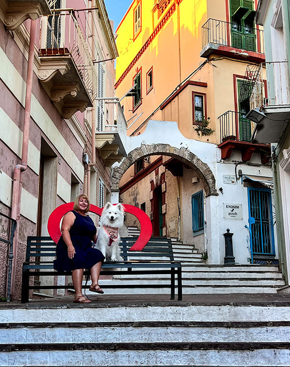 Jennifer and Coco sit in a heart frame on the steps of a steep street in Carloforte, Sardinia