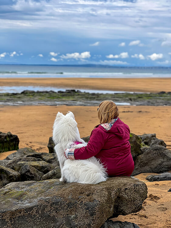 Jennifer and Coco sit on a rock on Fanore Beach watching the Atlantic Ocean in County Clare, Ireland