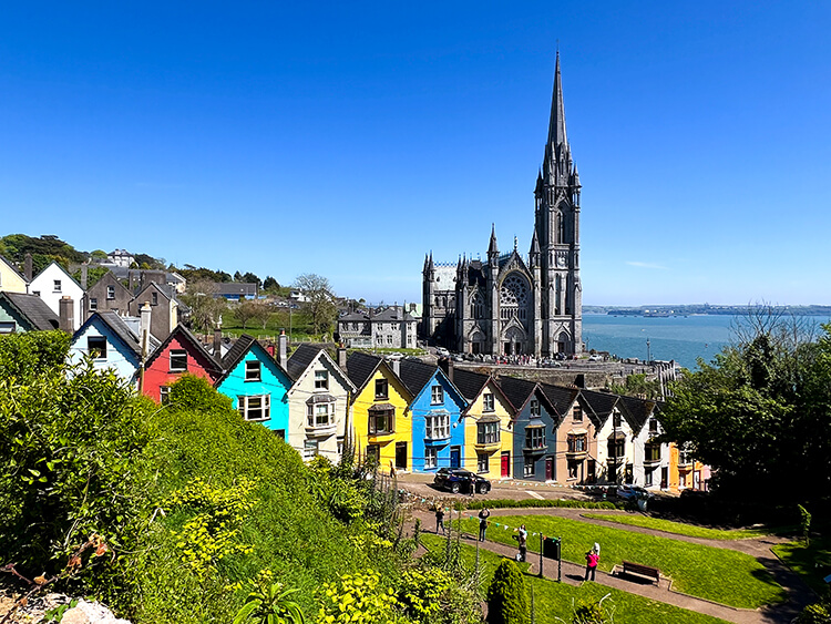 The candy-colored "Deck of Cards" houses lined up along a steep street in Cobh with a view of St. Colman's Cathedral and Cork Harbour behind