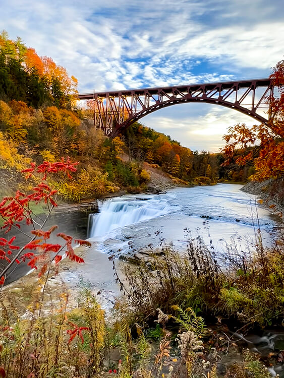 Viewpoint standing on the top of the drop of the Upper Falls waterfall with the railroad bridge behind and falls colors in the canyon at Letchworth State Park