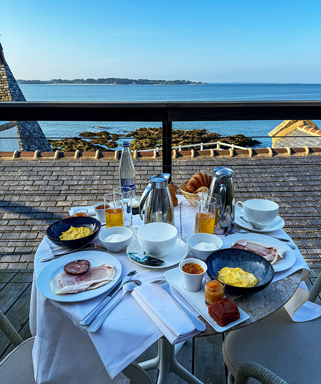 Breakfast of scrambled eggs, ham, pastries, coffee and juice on the terrace with a sea view
