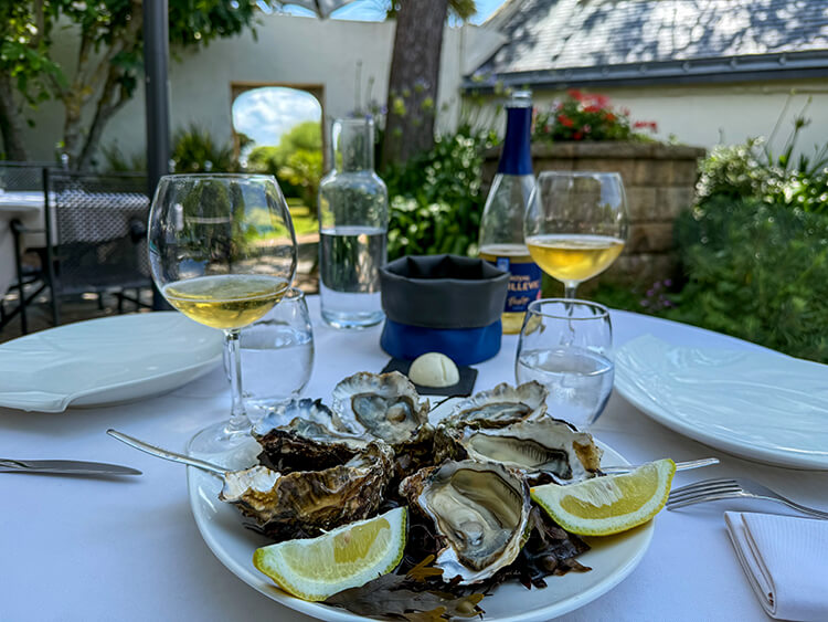 A plate of half a dozen Breton oysters served with lemon wedges in the garden of Le Bar à Coquillages at Domaine de Rochevilaine