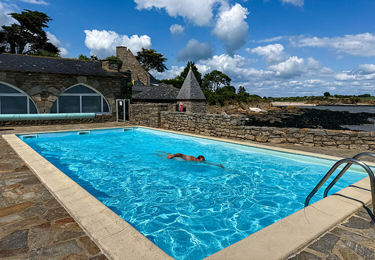 Tim swims in the outdoor pool with a view of the rocky coast and sand beach at Domaine de Rochevilaine