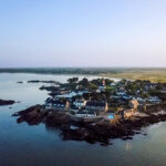 Drone aerial photo of the Domaine de Rochevilaine complex of historic buildings with the red and white striped lighthouse of Pen Lan in the background