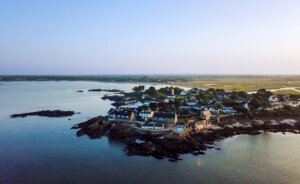 Drone aerial photo of the Domaine de Rochevilaine complex of historic buildings with the red and white striped lighthouse of Pen Lan in the background