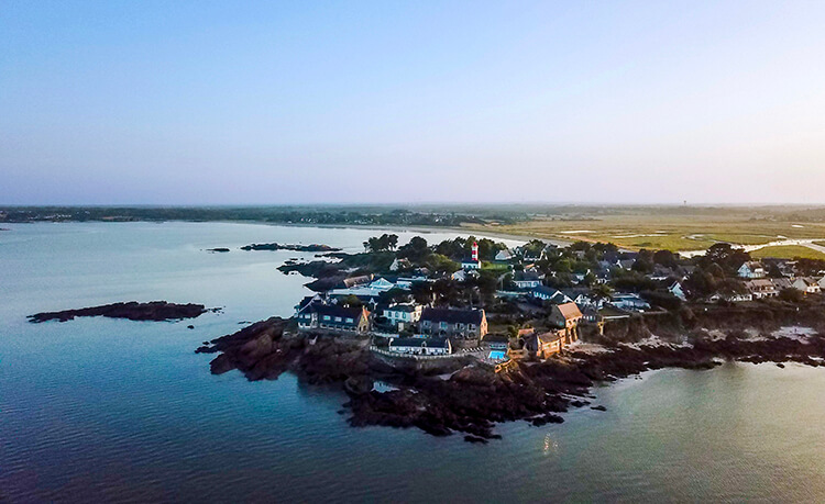 Drone aerial photo of the Domaine de Rochevilaine complex of historic buildings with the red and white striped lighthouse of Pen Lan in the background