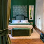 The bedroom of a junior suite at Hotel La Gemma with emerald green walls, botanical palm leaf wallpaper, bedding and curtains in rich emerald velvet