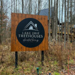 Lake Erie Treehouses welcome sign with a treehouse visible behind nestled in the forest