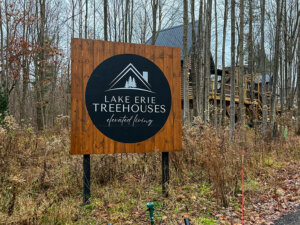 Lake Erie Treehouses welcome sign with a treehouse visible behind nestled in the forest