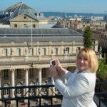 Jennifer holds her iPhone to take a photo of the Bordeaux skyline from the rooftop of the Grand Hotel