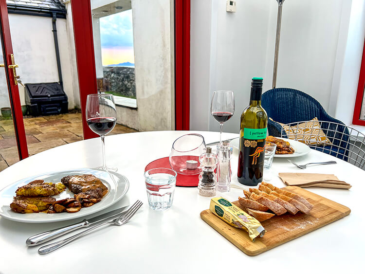 Steaks, mushrooms, smash potatoes, sourdough bread, butter and wine set at a table in the conservatory for dinner at Clare Island Lighthouse
