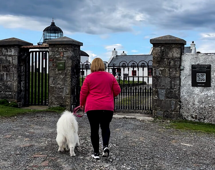 Jennifer and Coco walk to the gated entrance of the stone walled grounds of Clare Island Lighthouse