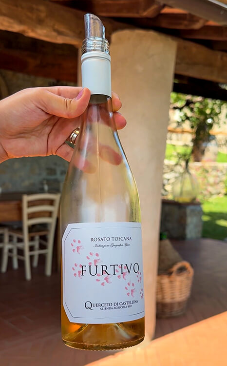 A bottle of Furtivo held up to show the white label with pink paw prints of the winery dog, Elliott, at Querceto di Castellina